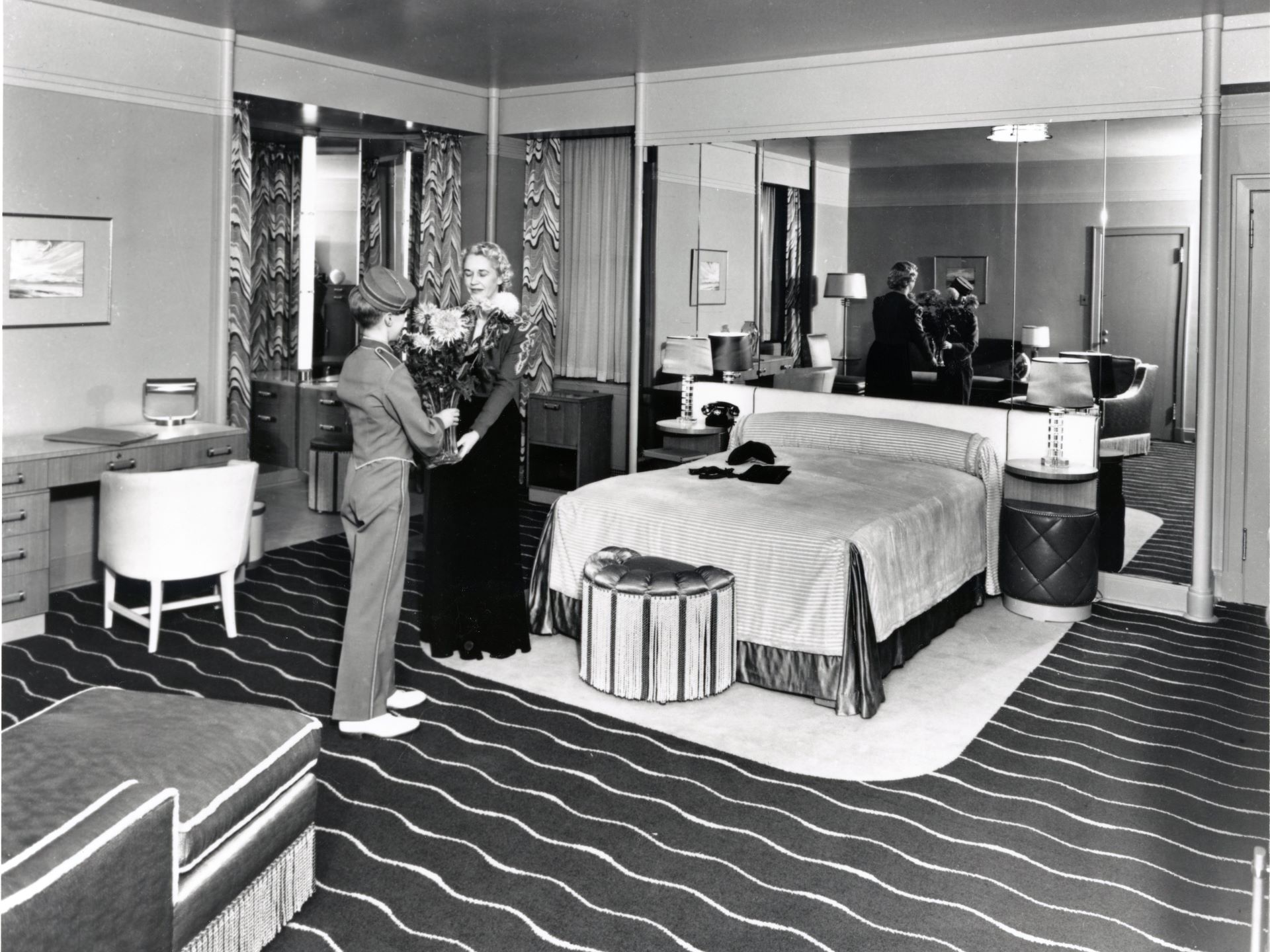 Photo of bell boy handing a guest a bouquet of flowers in an art moderne designed guest room circa 1939