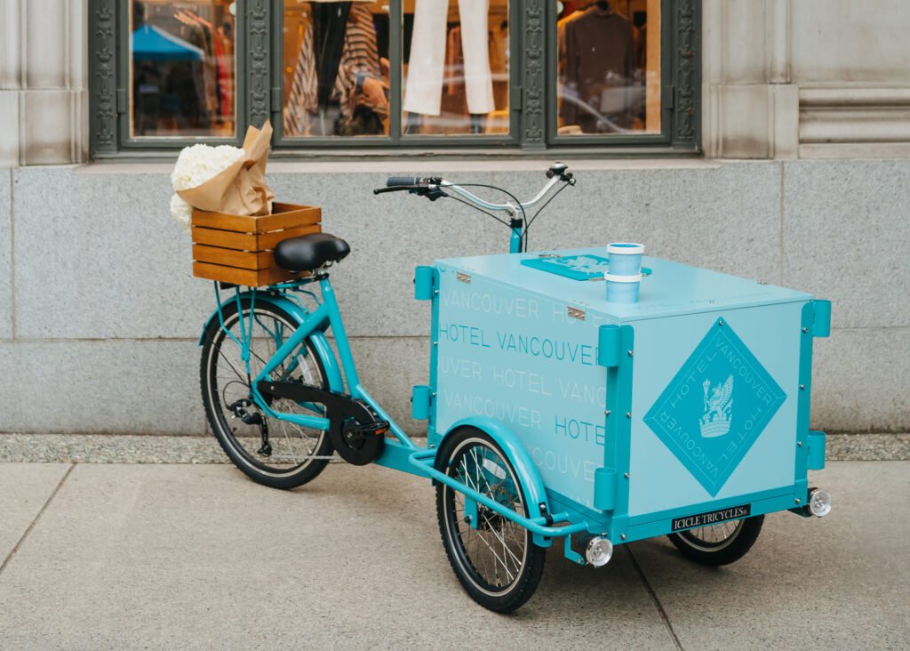 Teal ice cream tricycle with a wooden crate on the back with flowers in it