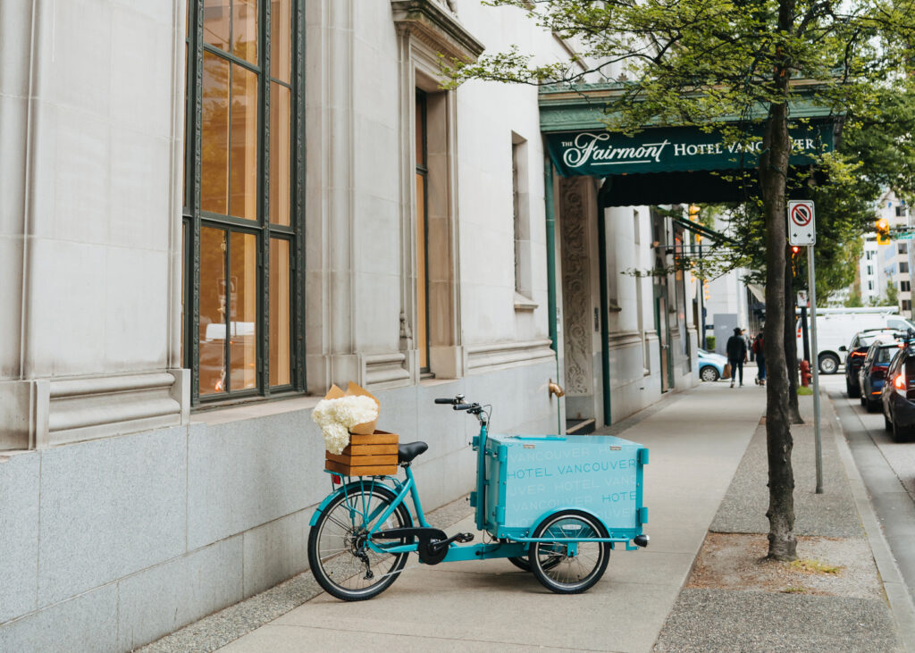 Teal ice cream tricycle on a sidewalk with Hotel Vancouver entrance in the background