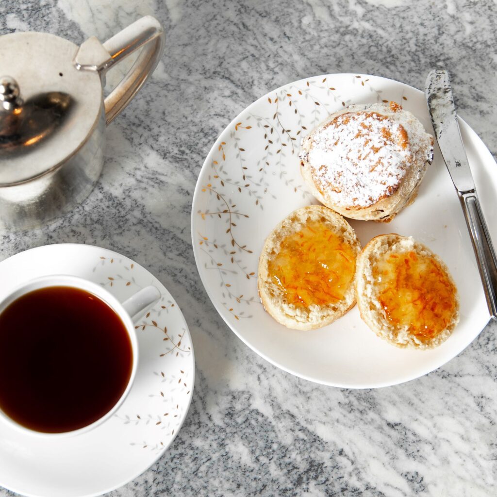 Tea scones on a plate topped with marmalade, with a cup of tea next to them.