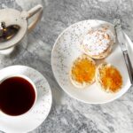 Tea scones on a plate topped with marmalade, with a cup of tea next to them.