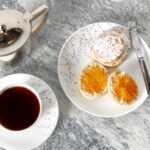 Tea scones on a plate topped with marmalade, with a cup of tea next to them.