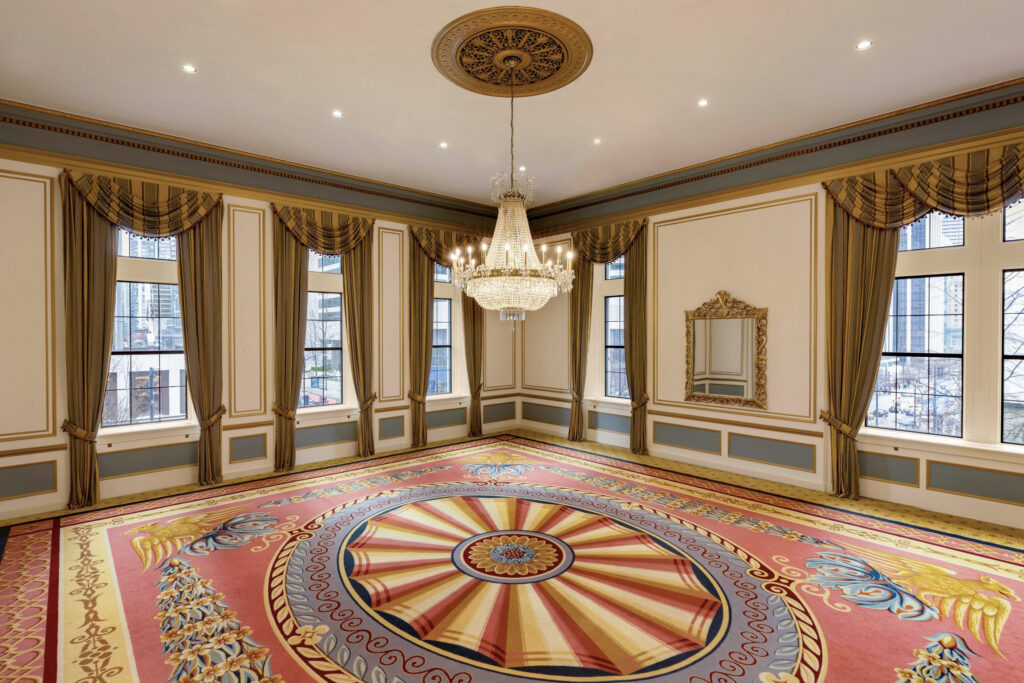 The Boardroom venue in Fairmont Hotel Vancouver showing a crystal chandelier hanging in the middle with large windows in the background.