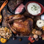 A whole turkey on a wooden cutting board with traditional Thanksgiving dinner sides.