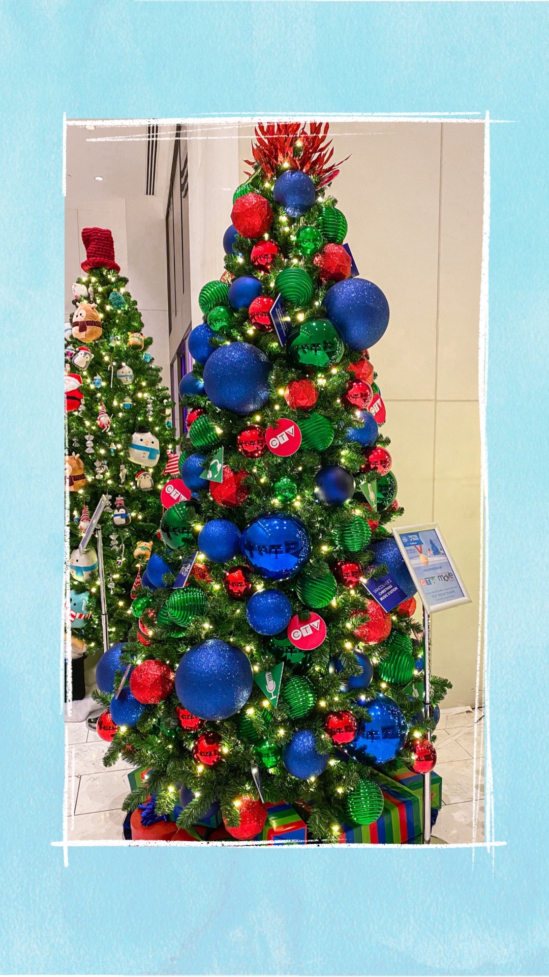 A holiday tree decorated with blue, red, and green ornaments for the BCCHF Festival of Trees