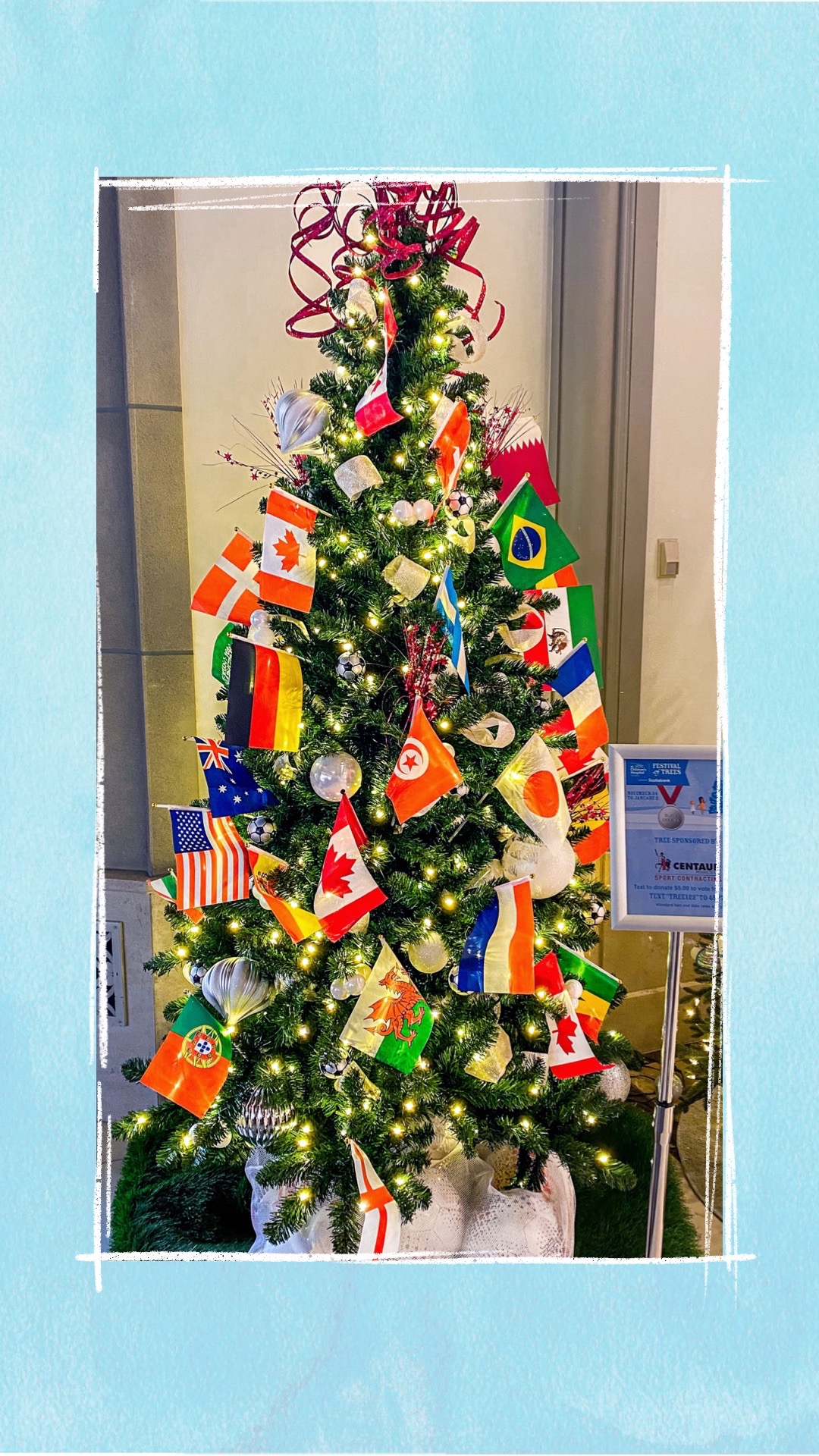 A holiday tree decorated with country flags and a bag of soccer balls underneath for the BCCHF Festival of Trees