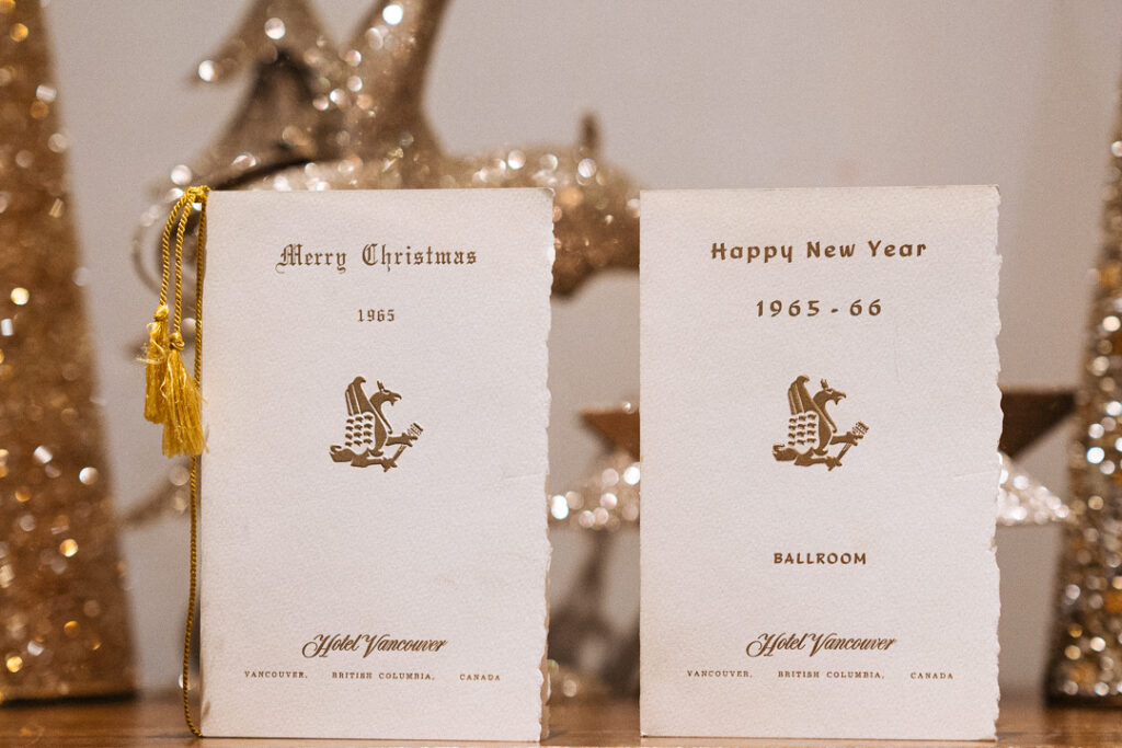 Two Hotel Vancouver vintage holiday menus from 1965 sitting on a table with decorations behind them.